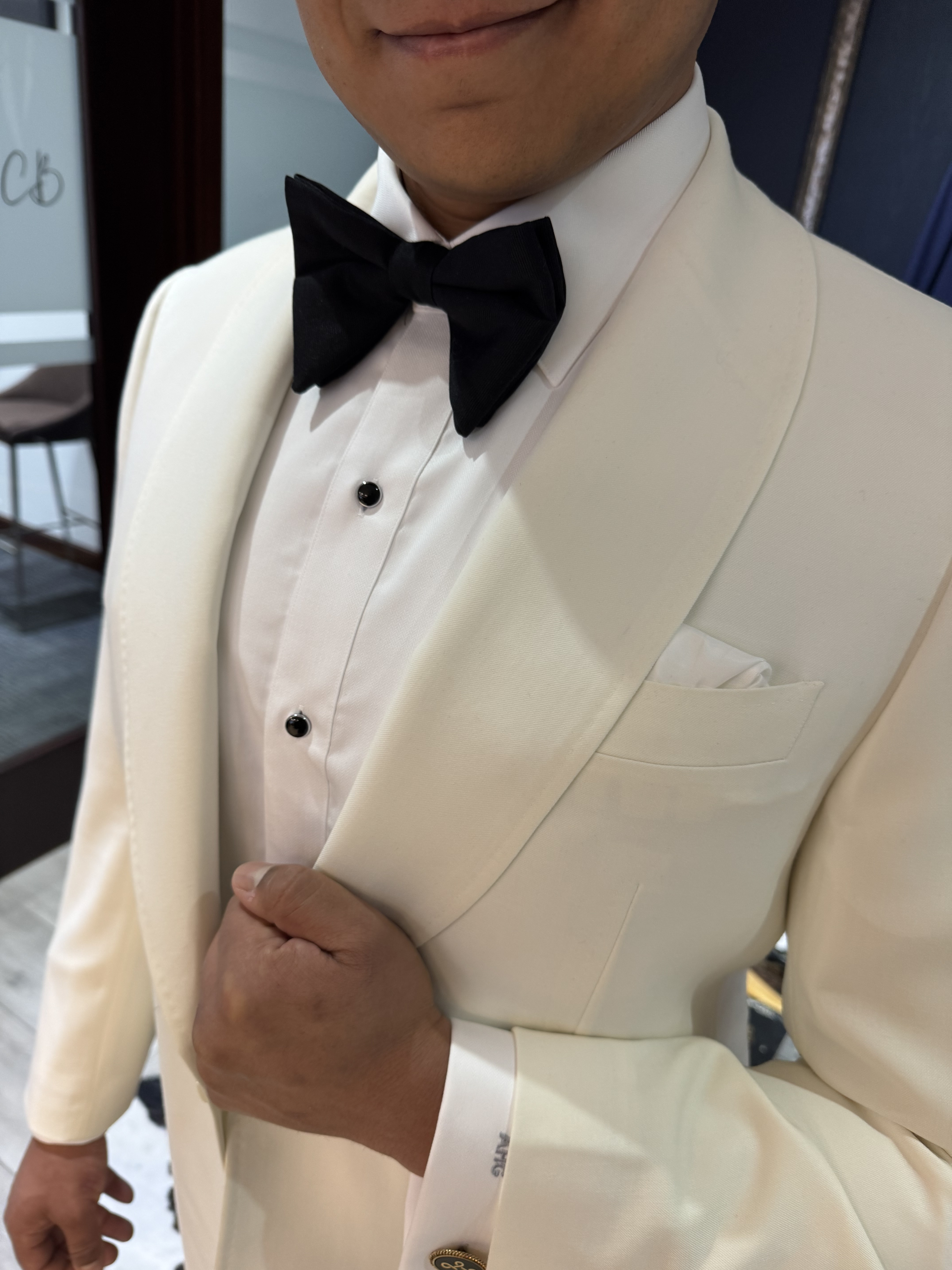Close-up of a custom cream dinner jacket with shawl lapels, black bow tie, and monogrammed sleeve cuff at Bespoke By CB Miami