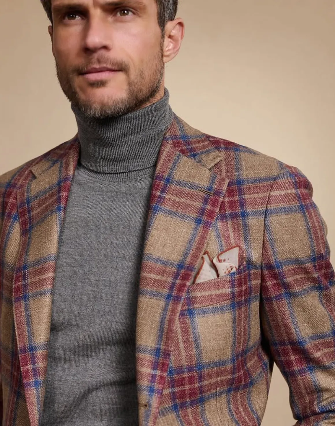 Man wearing a brown and blue plaid sport jacket over a grey turtleneck with a pocket square, showcasing winter layering for men