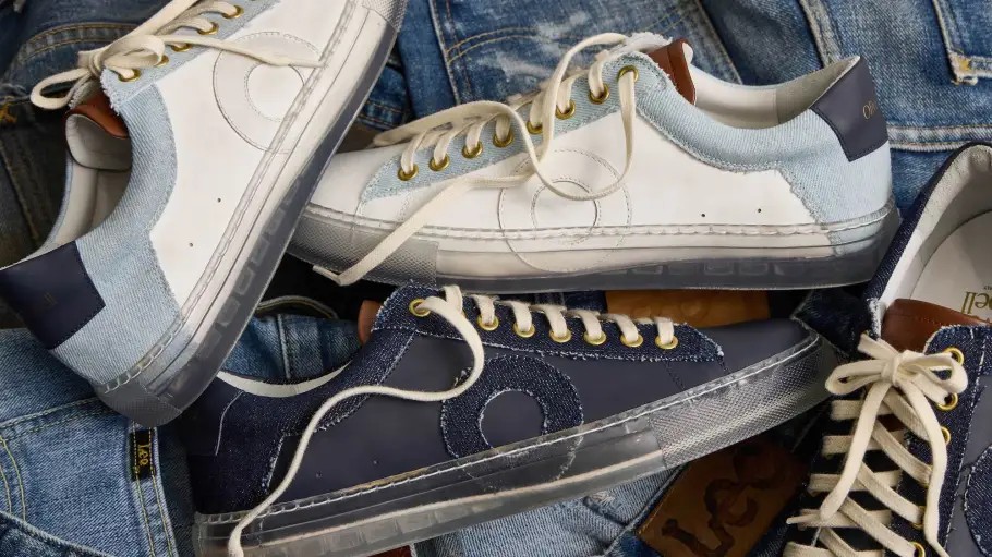 Oliver Cabell Low 1 sneakers in white leather and navy suede flat lay on denim, showing mixed materials, gold eyelets, and translucent rubber soles