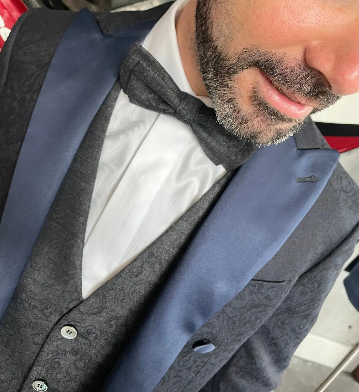 Close-up detail of navy morning coat satin peak lapel with charcoal paisley waistcoat and matching bow tie