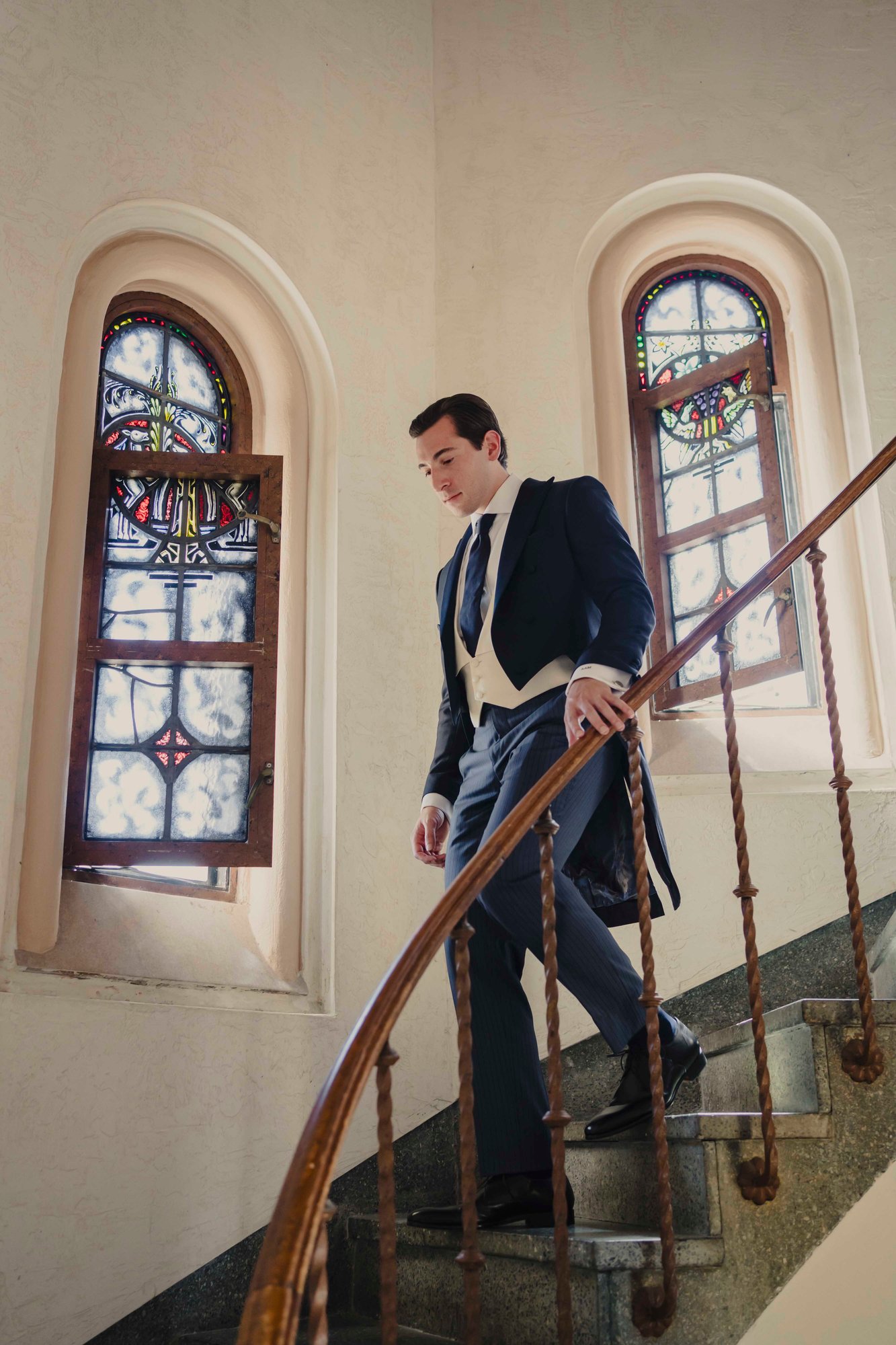 Navy bespoke morning coat shown in motion descending staircase — demonstrating the elegant tail movement of proper morning dress