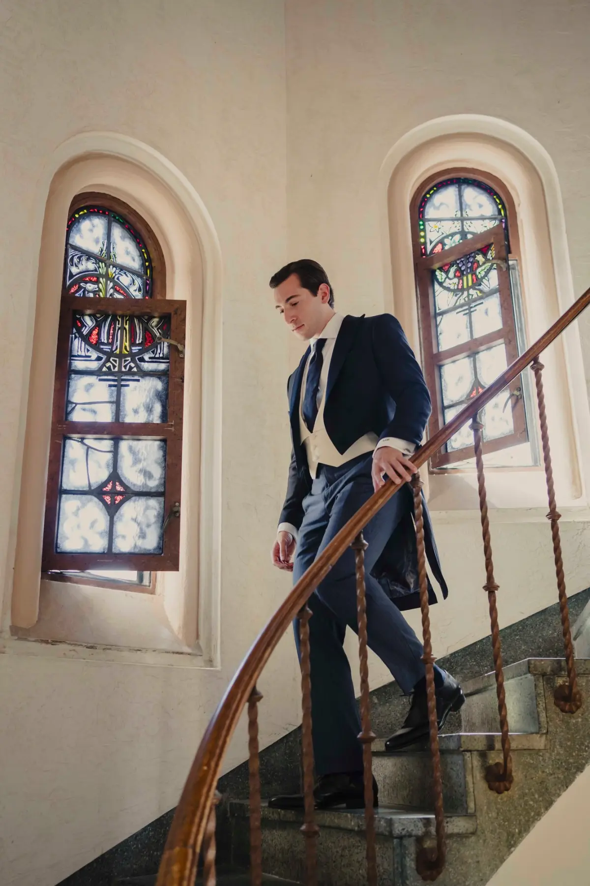 Navy bespoke morning coat shown in motion descending staircase — demonstrating the elegant tail movement of proper morning dress