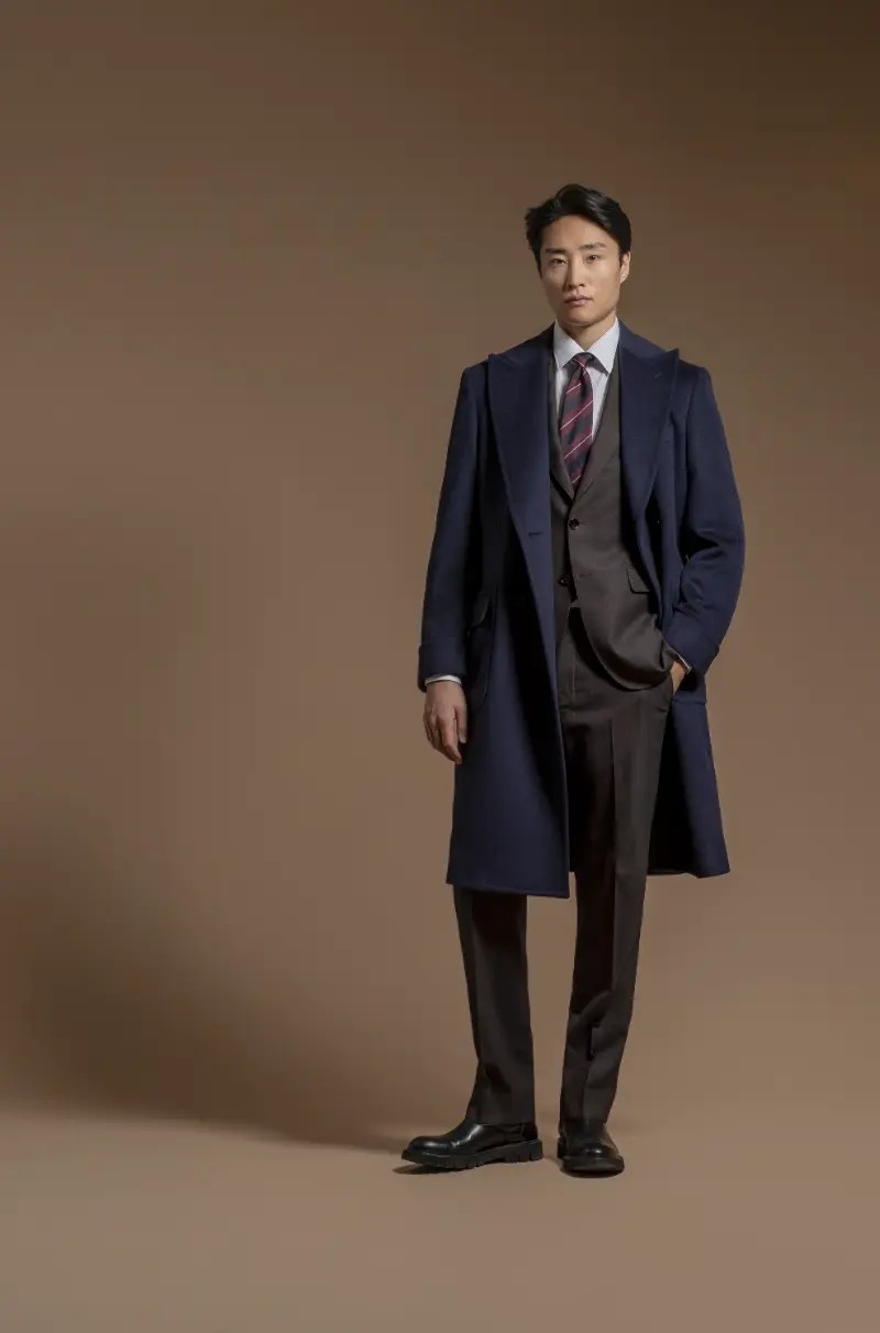 Navy wool overcoat draped over a dark brown three-piece suit with burgundy tie