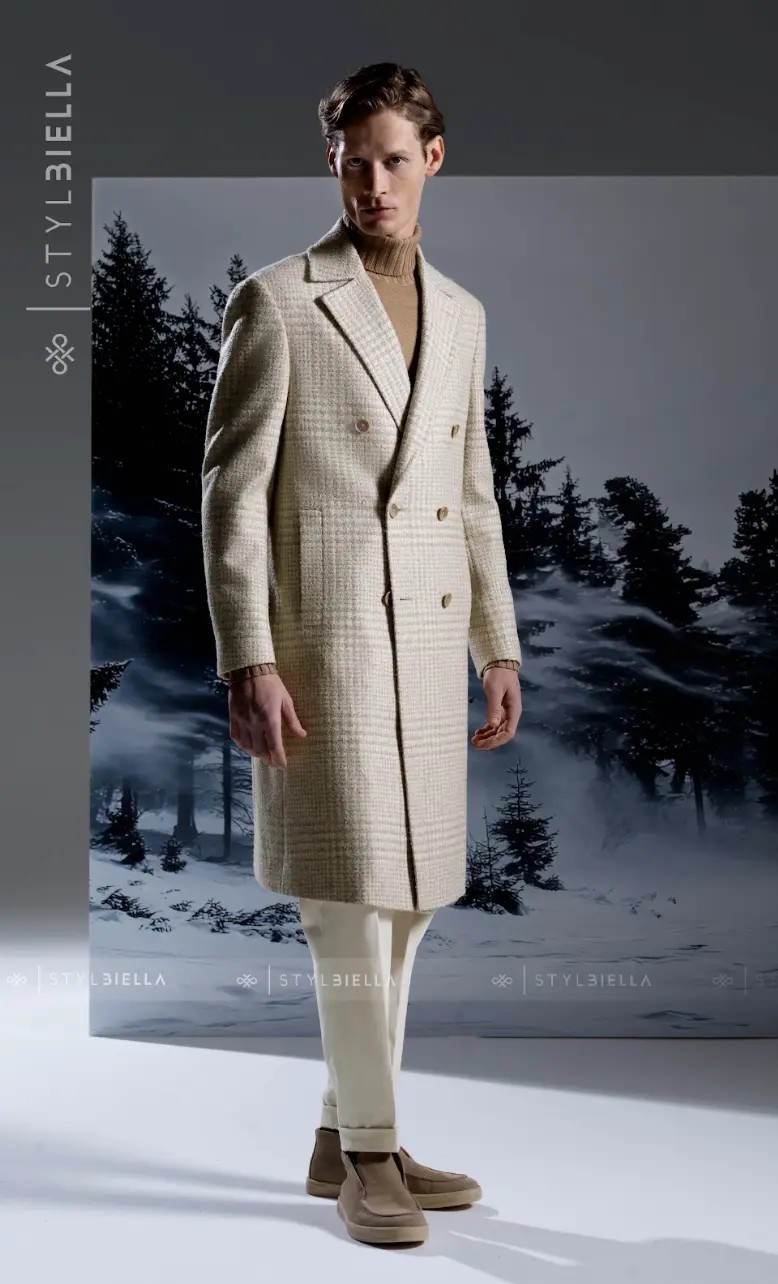 Cream plaid double-breasted overcoat with tan buttons over a turtleneck against snowy backdrop