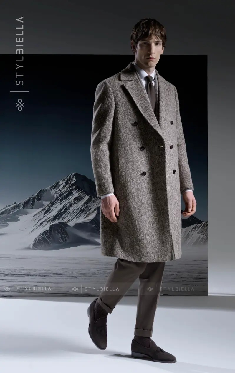 Grey herringbone double-breasted overcoat with white shirt and brown tie against mountain landscape