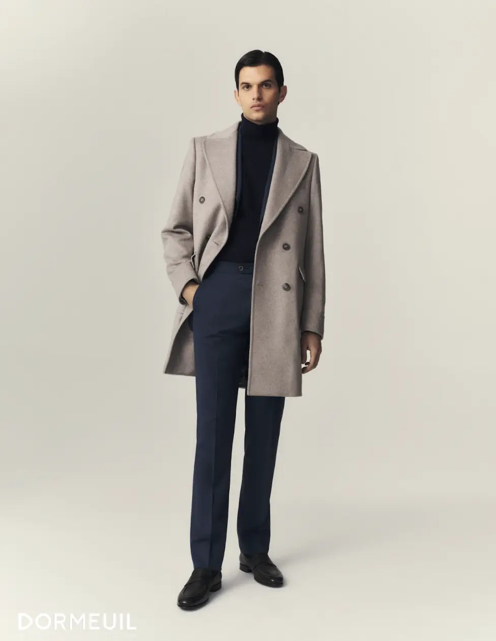Oatmeal double-breasted overcoat over navy turtleneck showing full body styling in studio