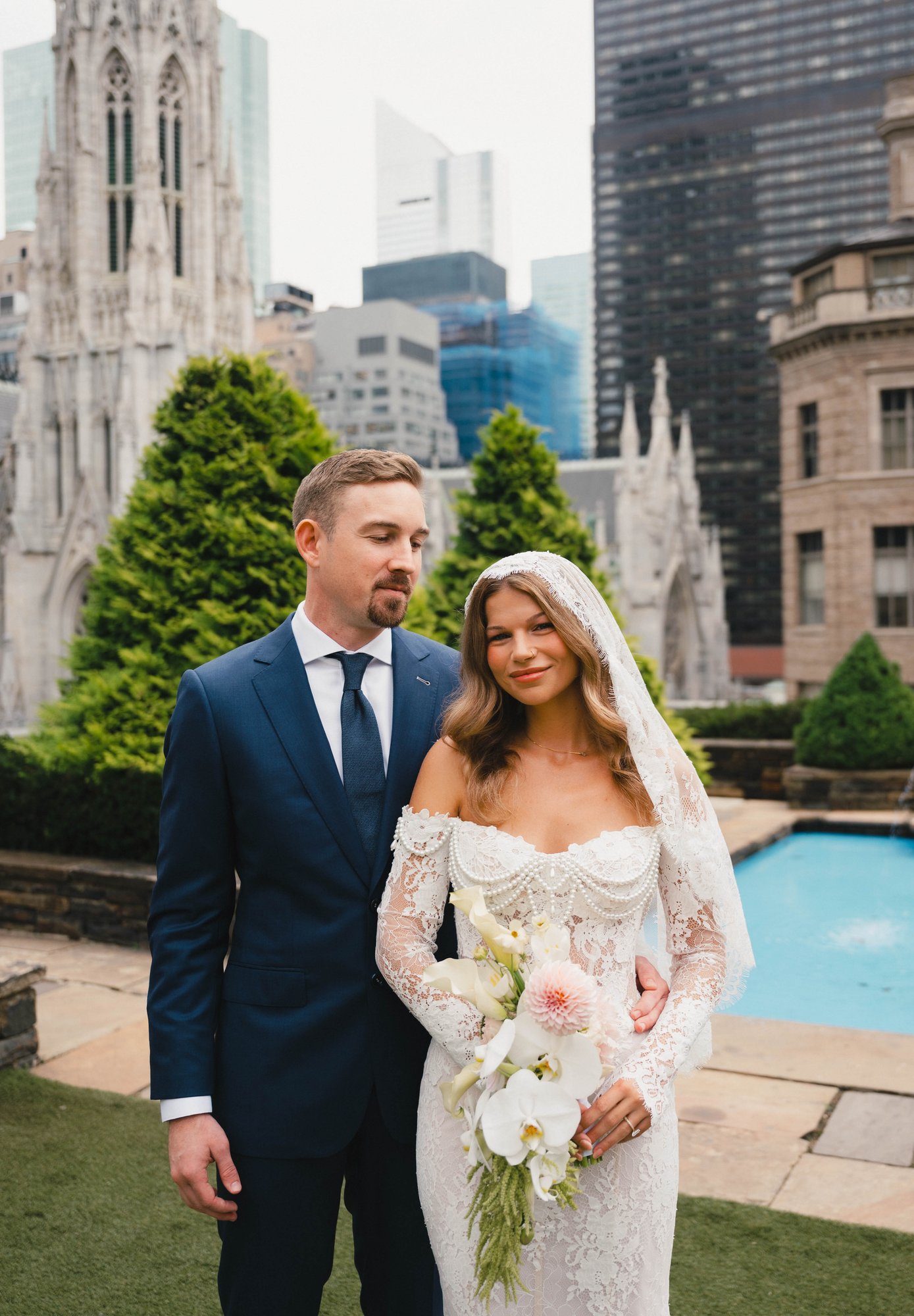 Joseph and his bride in an urban setting with historical architecture, showing the full silhouette of the custom wedding suit.