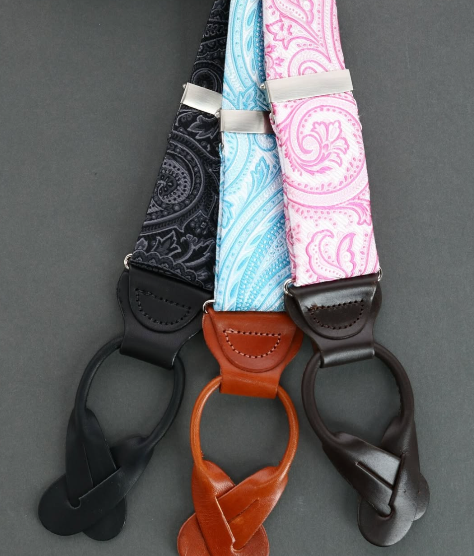 Custom suits: Three paisley suspenders in black, light blue and pink with black, tan and dark brown leather button tabs on a grey background