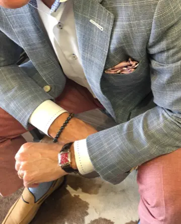 Close-up styling detail of a grey patterned blazer with pocket square, showcasing bespoke tailoring and accessory pairing