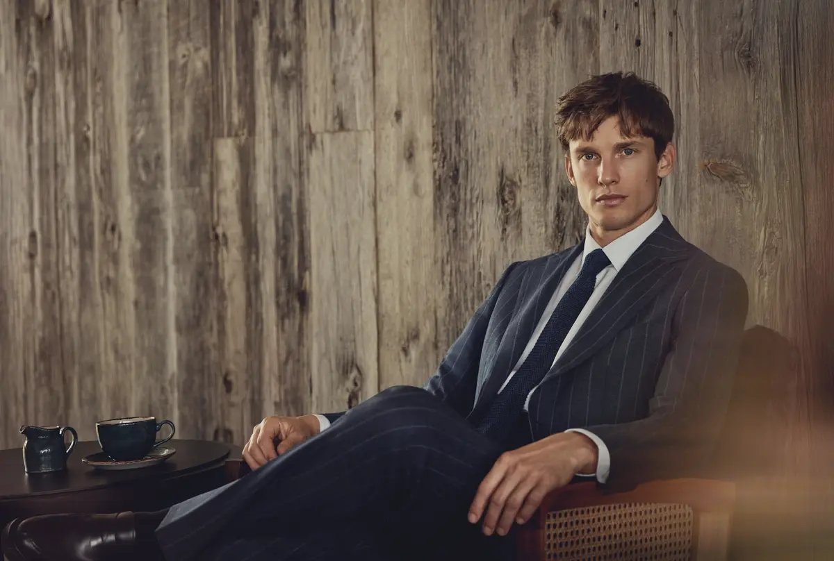 Navy pinstripe suit jacket with peak lapels worn indoors showcasing custom tailoring details