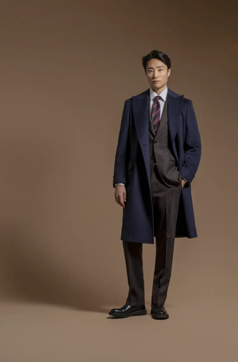 Navy wool overcoat draped over a dark brown three-piece suit with burgundy tie
