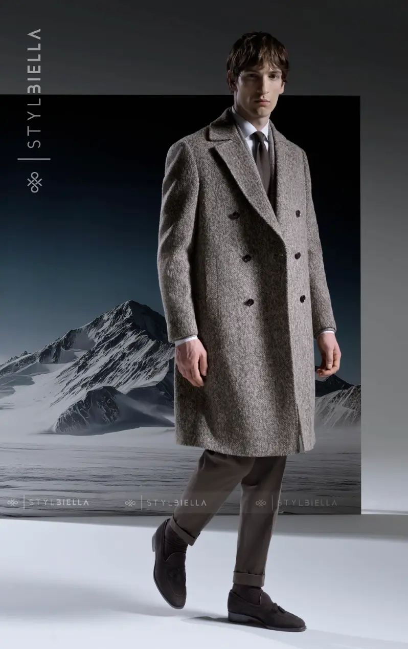 Grey herringbone double-breasted overcoat with white shirt and brown tie against mountain landscape