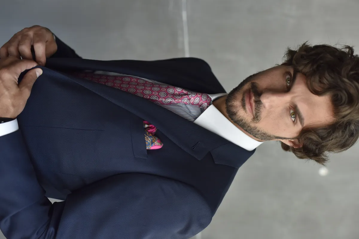 A navy custom suit worn against an urban concrete wall shows the sharp, professional look that Bespoke By CB creates for busy Miami professionals
