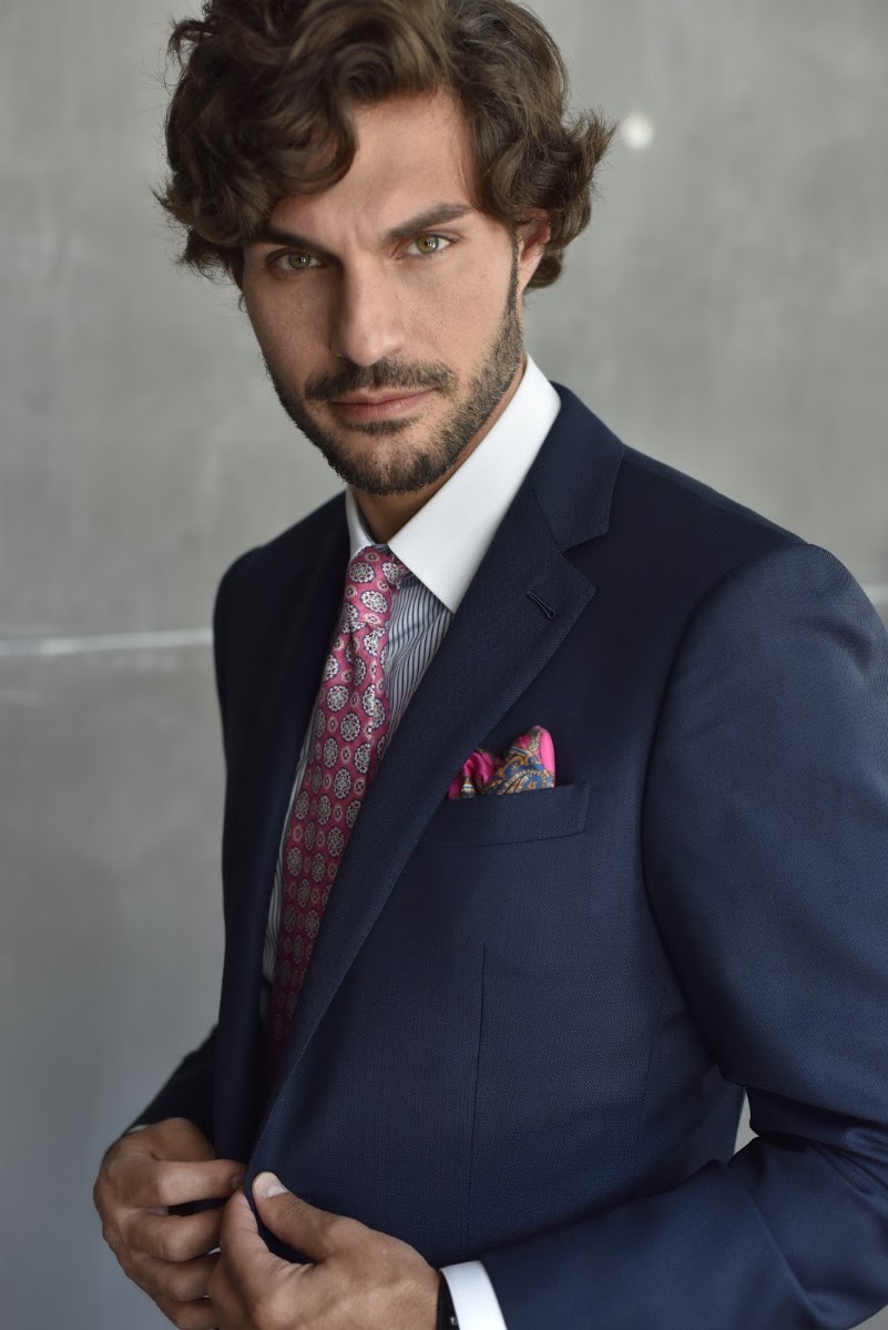 Man wearing a navy custom suit with pocket square standing against a concrete wall, demonstrating precise Miami tailoring fit