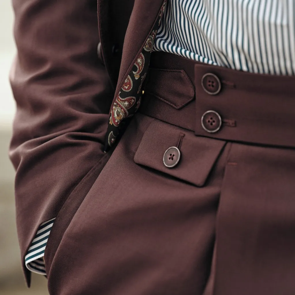 High-waisted burgundy trousers showing the waistband detail where side adjusters replace belts.