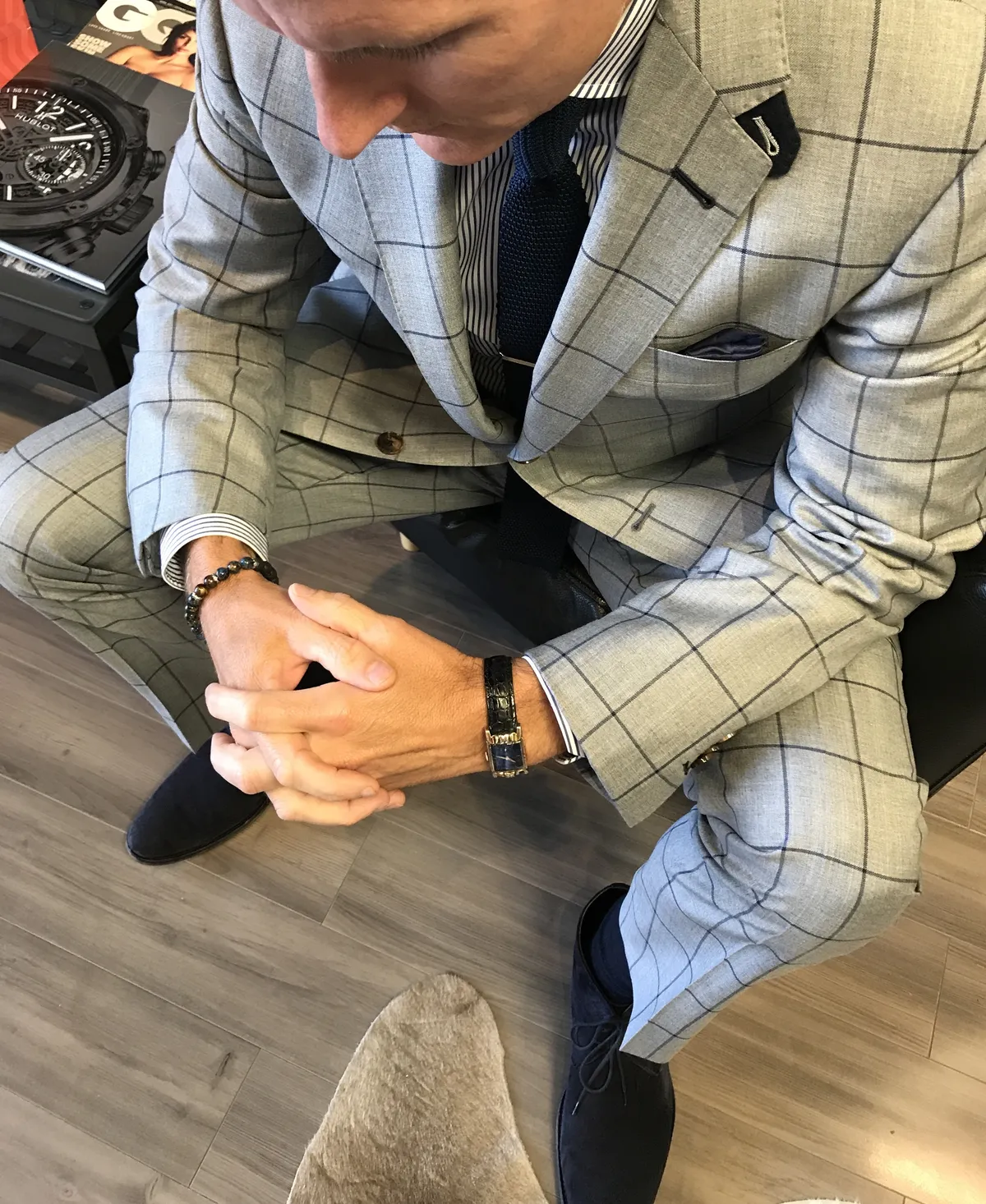 Light grey windowpane check custom suit worn seated with a navy tie and striped shirt by Bespoke By CB