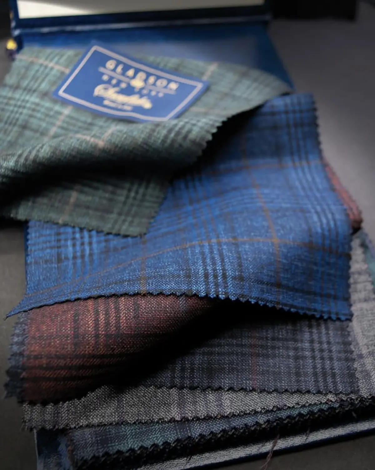 Gladson luxury fabric swatches showing the same premium mills that supply both designer brands and bespoke tailors.