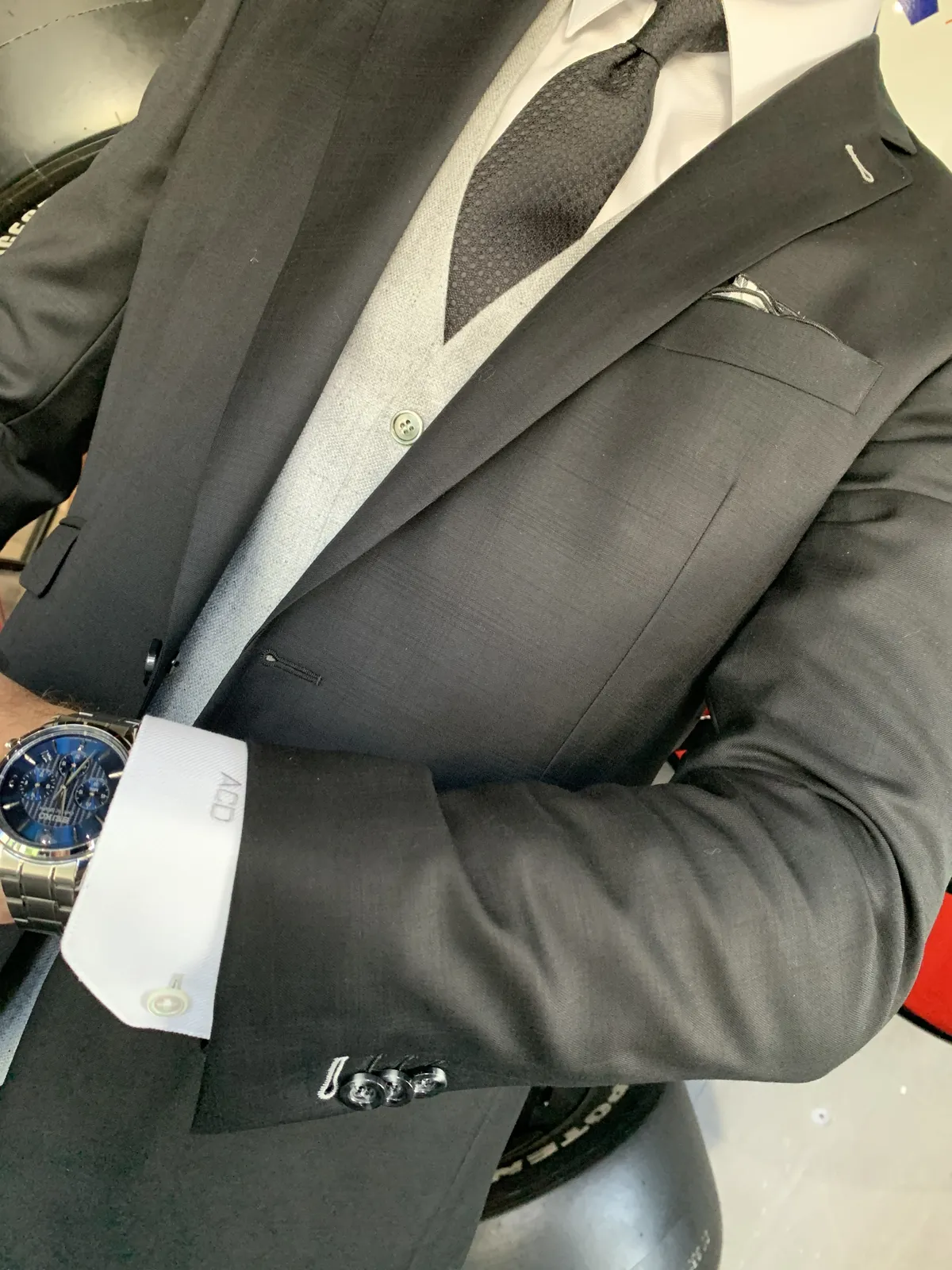Man wearing a charcoal suit with French cuffs, silver cufflinks, and a monogrammed shirt cuff.