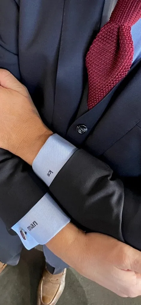 Close-up of a navy three-piece suit with a burgundy knit tie, pale blue monogrammed shirt cuffs and tan shoes