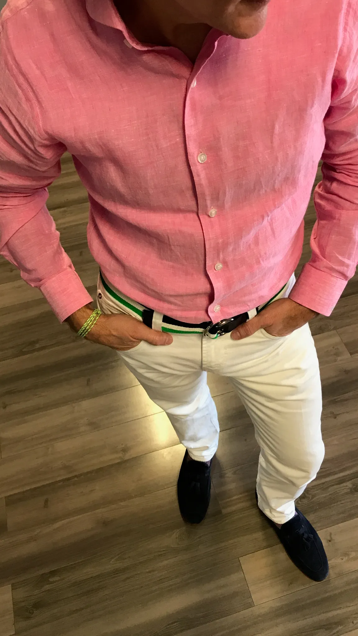 Man wearing a pink button-down shirt, white trousers, a green and white striped belt and dark loafers