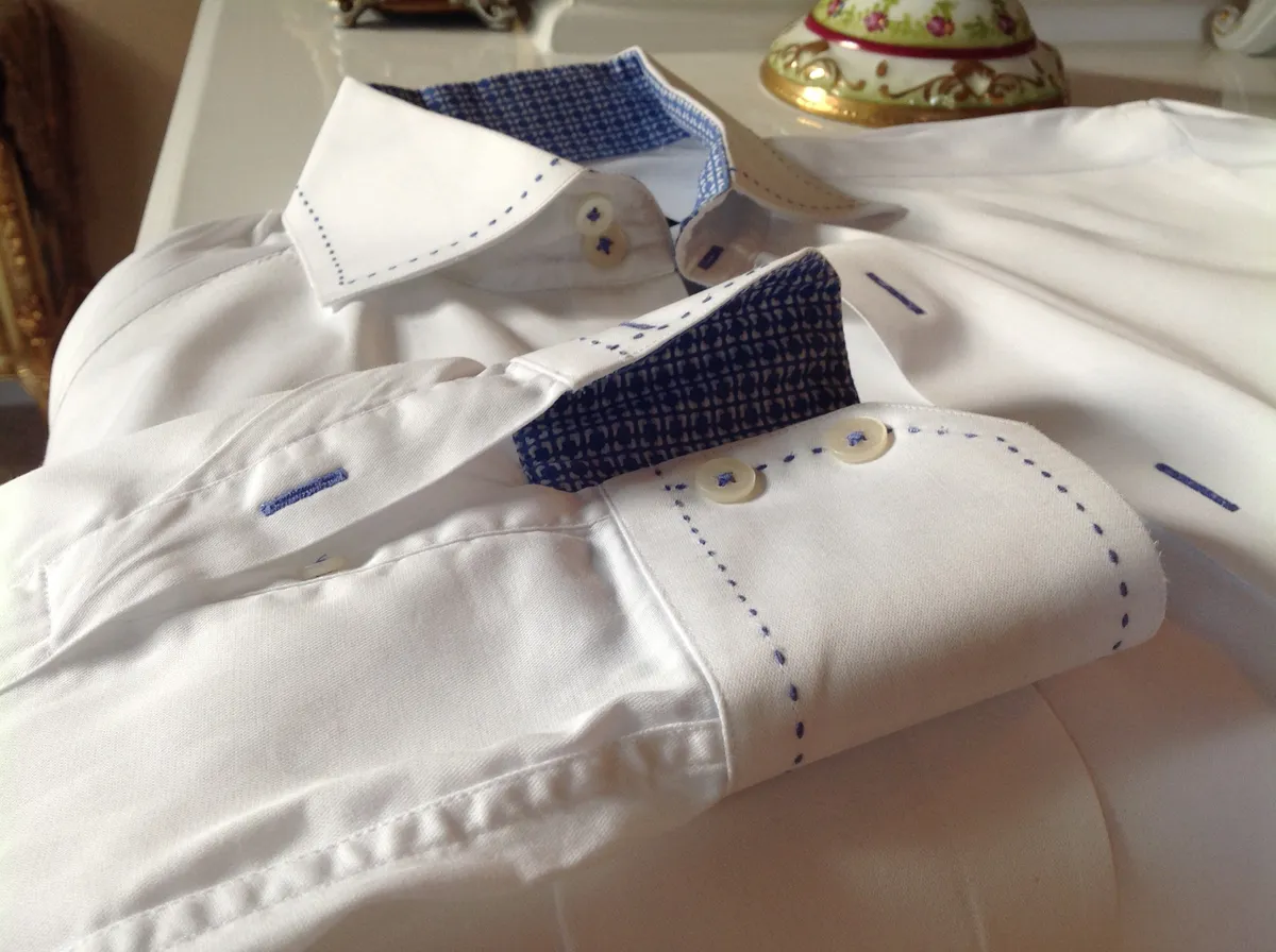 White custom shirt with blue contrast pick-stitching on the collar and a patterned inner lining.