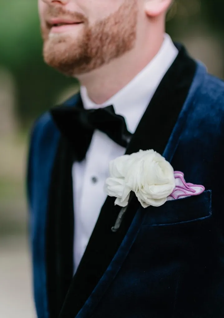 Close-up of a navy velvet dinner jacket with satin lapels and a floral boutonniere, custom formalwear by Bespoke By CB