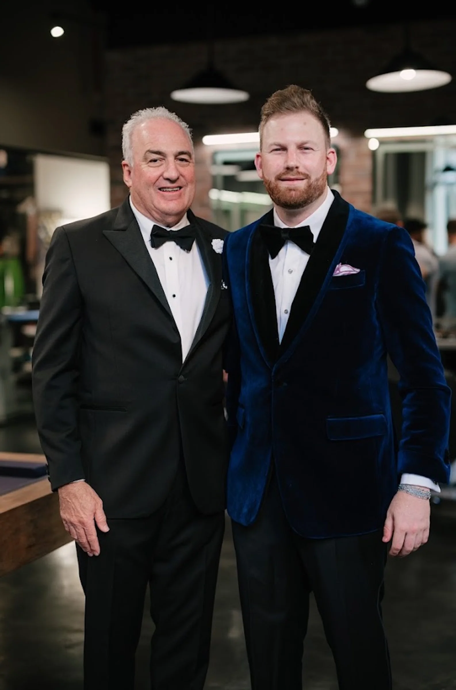 Two men in tuxedos with visible French cuffs and silver cufflinks in a formal lounge setting.
