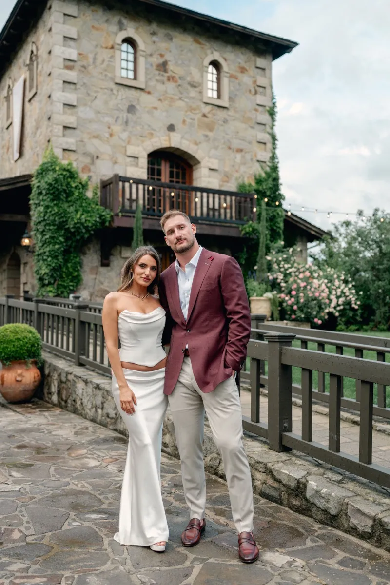 Joey Bosa and Amanda Kassdikian on cobblestone path at estate, groom in burgundy custom blazer by Bespoke By CB